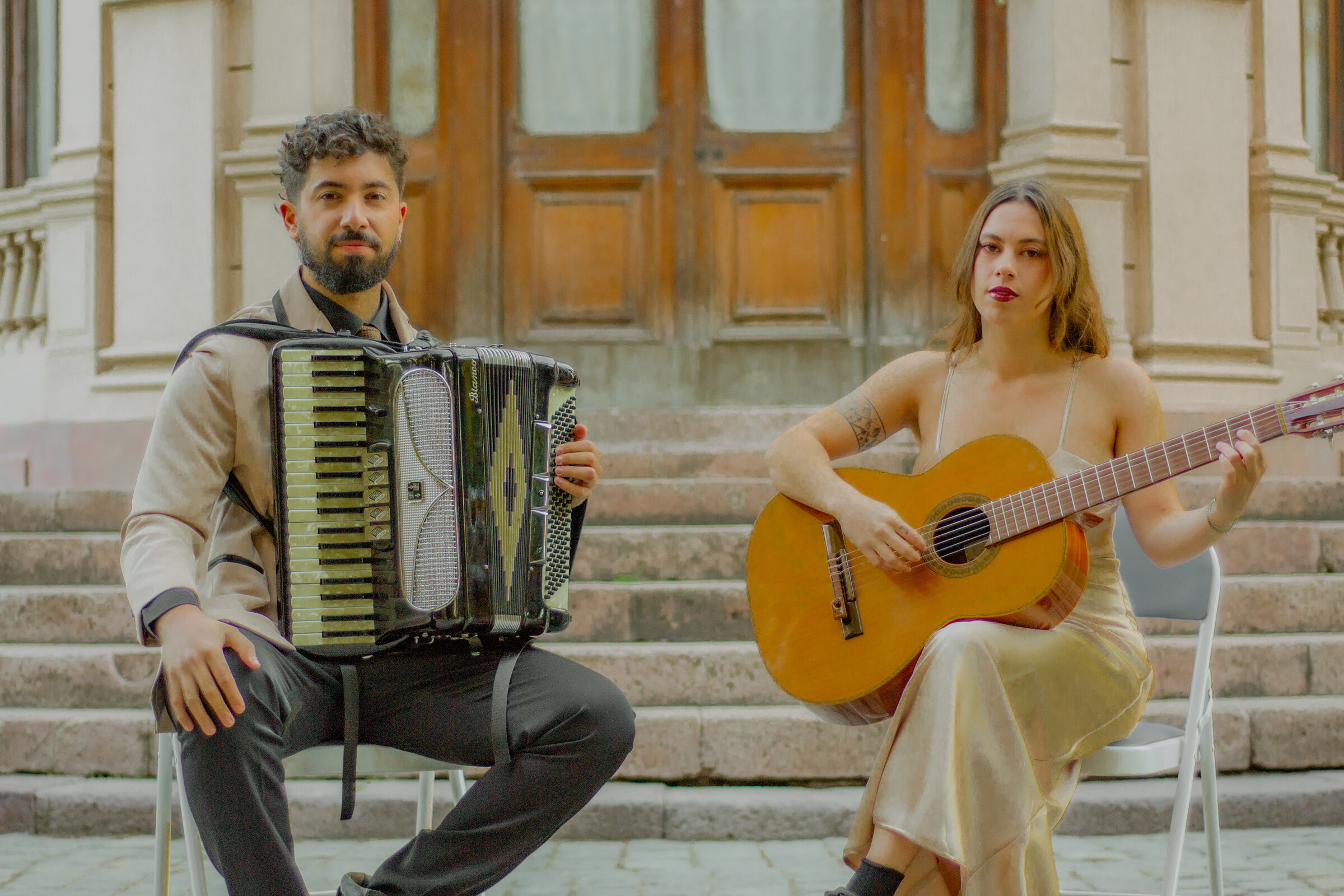 El Dúo Amores de Chile tocando guitarra y acordeón, sentados en las escalinatas del Palacio Cousiño.
