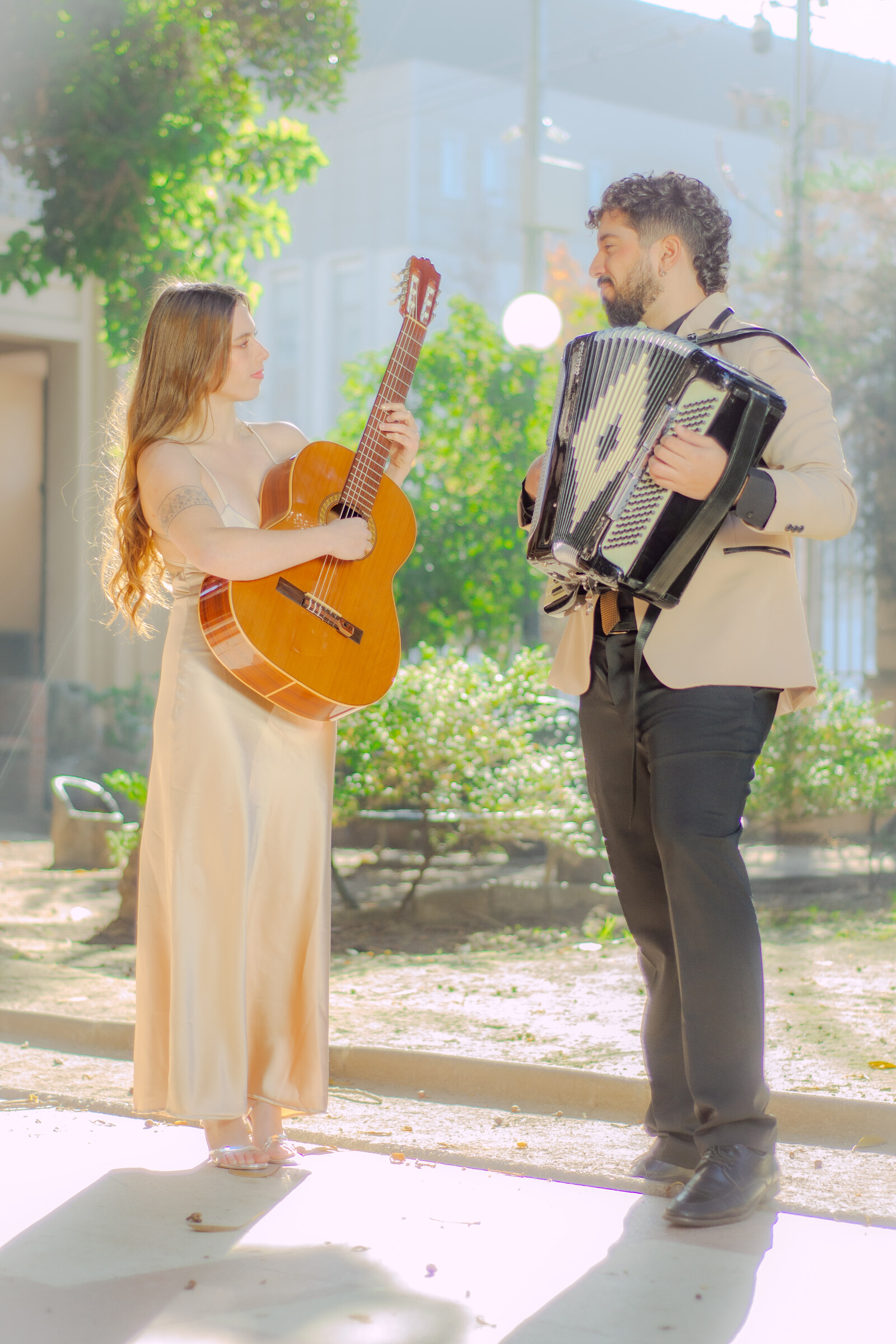 Dúo Amores de Chile tocando guitarra y acordeón, mirándose con complicidad en un jardín.